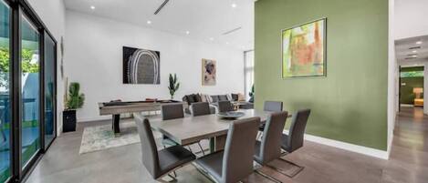 A modern dining area with a large table and chairs, a green accent wall, and artwork.