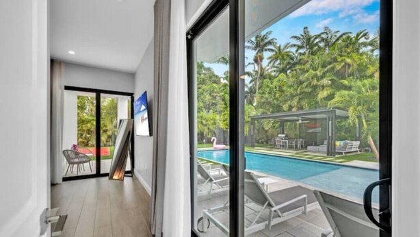 Habitació d'hotel moderna amb una porta de vidre que dona a un balcó amb piscina i palmeres.