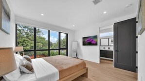 Un dormitorio moderno con una cama grande, un televisor en la pared y vistas a zonas verdes.