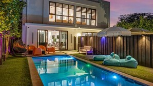 Una casa moderna de dos pisos con piscina, mobiliario exterior y cerca de madera.