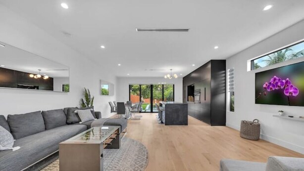 Una sala moderna con un sofá gris, una mesa de centro de vidrio y un televisor de pantalla plana montado en la pared.