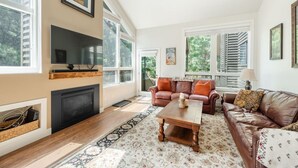 A spacious living room with a fireplace, leather sofas, a coffee table, and large windows offering a view of greenery. - Bright & Cozy Getaway (Park City)