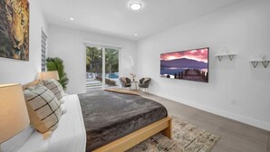 A modern bedroom with a large bed, a TV, and a painting of a sunset. - Waterfront Estate•7BR•Heated pool•Spa•BBQ•Basketball (Miami)