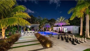 A luxurious outdoor area with a swimming pool, palm trees, and a chessboard. - Waterfront Estate•7BR•Heated pool•Spa•BBQ•Basketball (Miami)