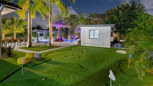 A well-maintained golf course with a putting green, palm trees, and a modern building with large windows. - Waterfront Estate•7BR•Heated pool•Spa•BBQ•Basketball (Miami)