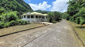 A two-story building with a balcony, surrounded by lush greenery and a mountainous backdrop. - Garden View Apartments - Managed by David & David Ltd (Roseau)