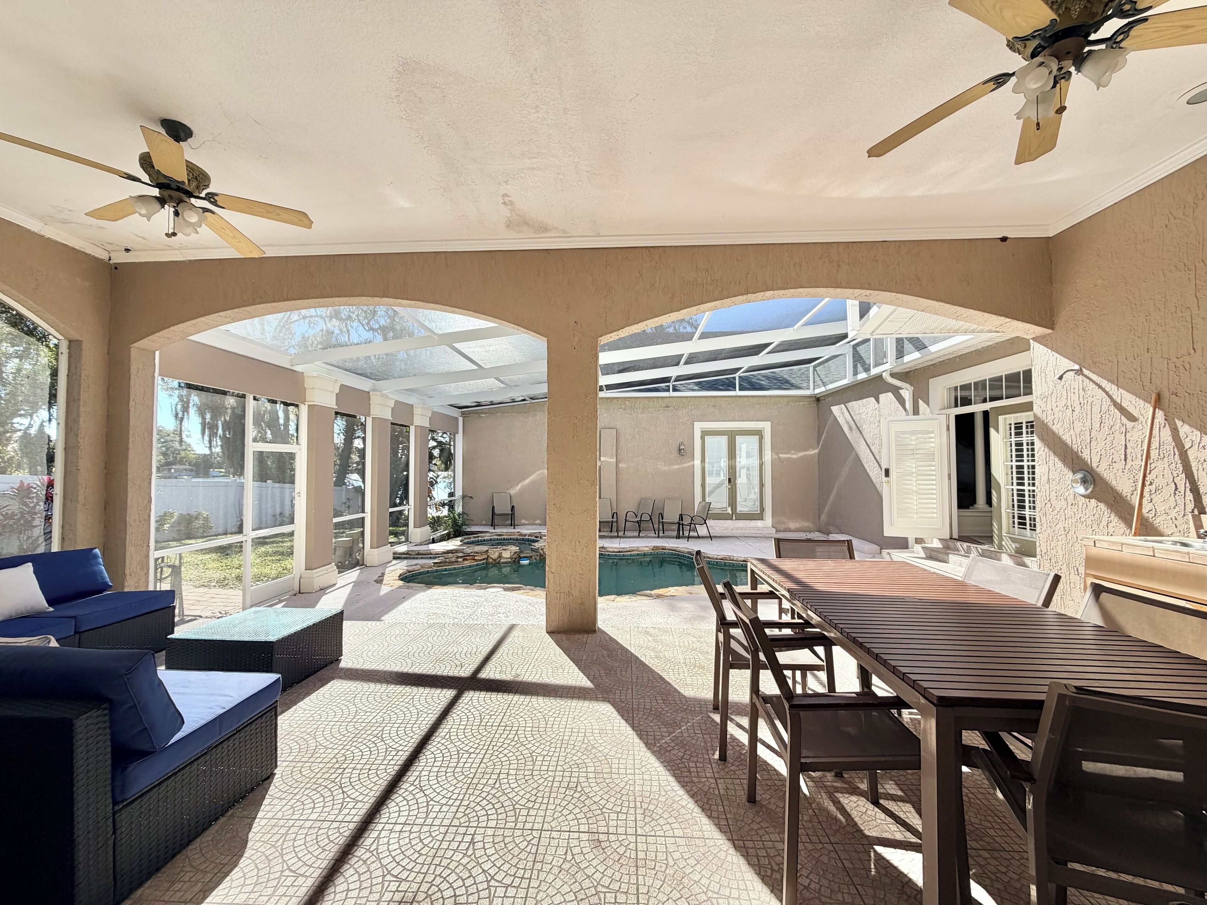 Une terrasse ensoleillée avec une piscine, du mobilier d’extérieur et un ventilateur de plafond.