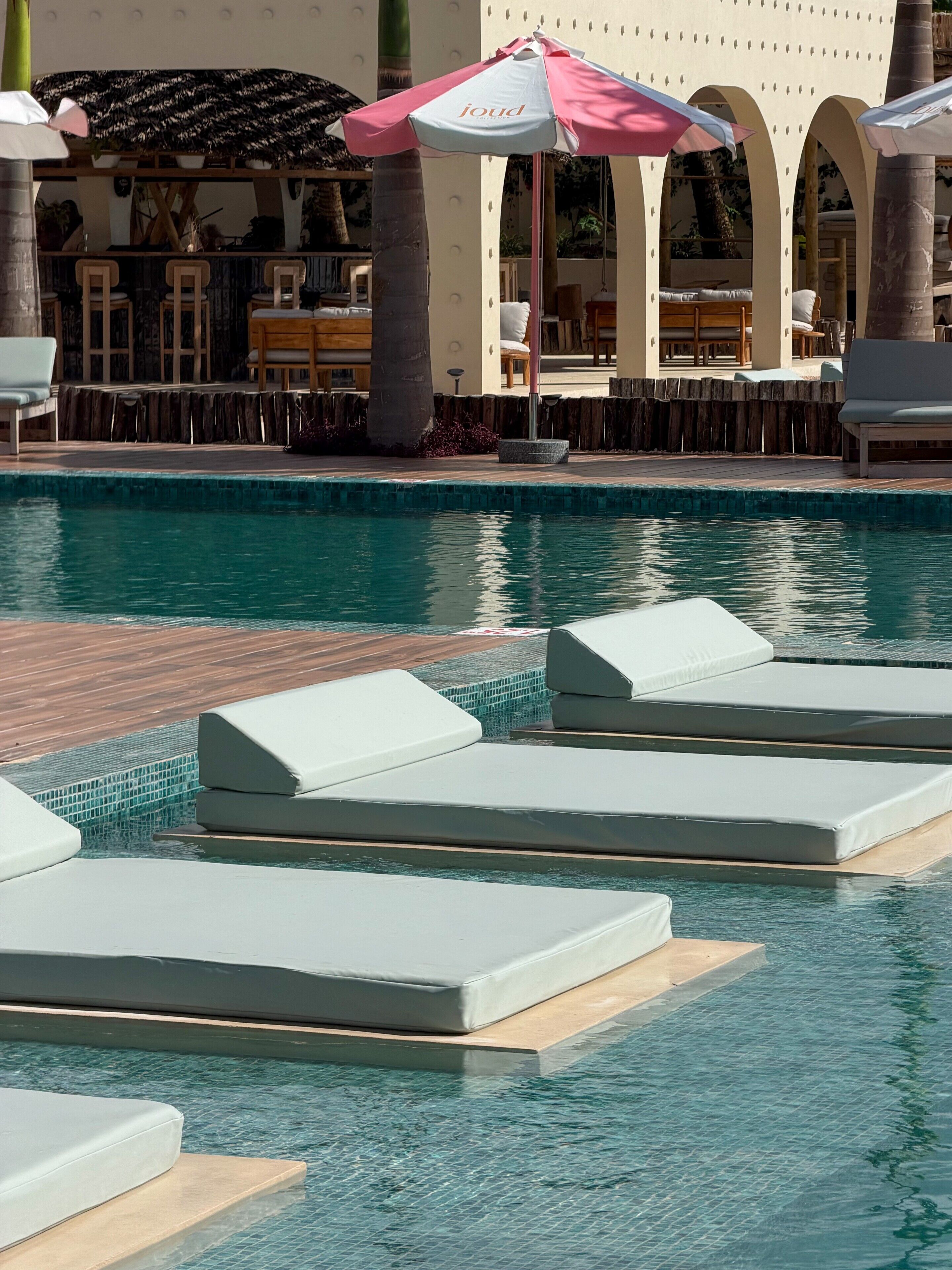 Una piscina al aire libre, sombrillas, sillones reclinables de piscina
