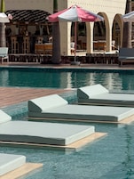Una piscina al aire libre, sombrillas, sillones reclinables de piscina