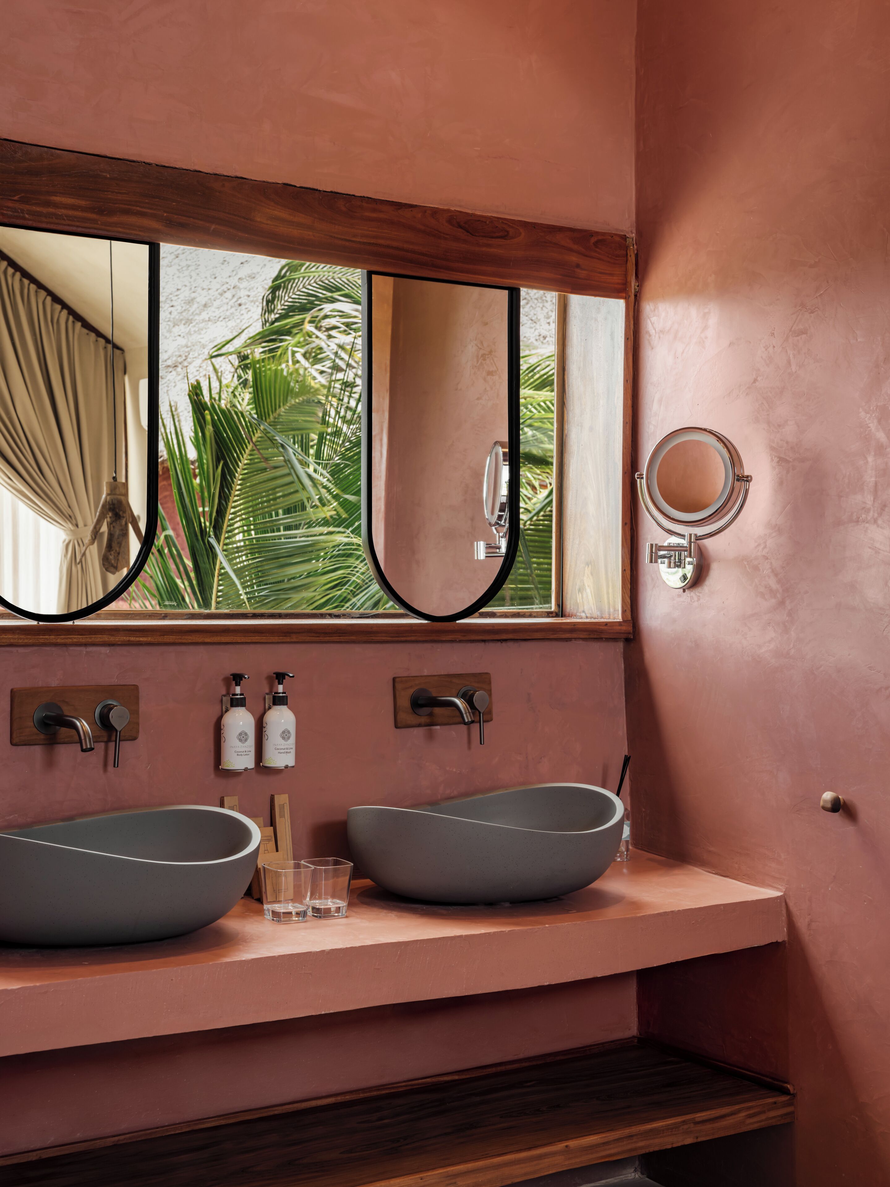 A bathroom with two vessel sinks, a large mirror, and a window with a view of greenery.
