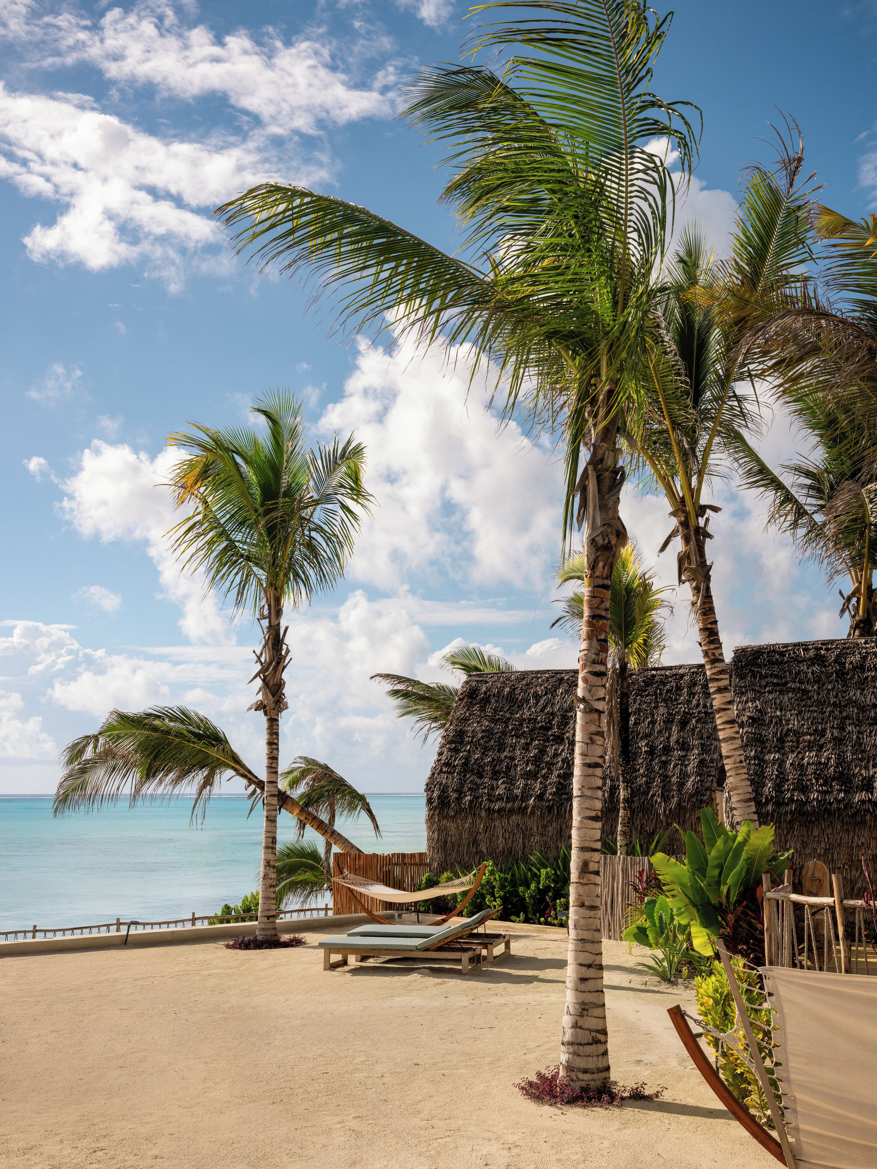 A beach with palm trees, a thatched hut, and a hammock.
