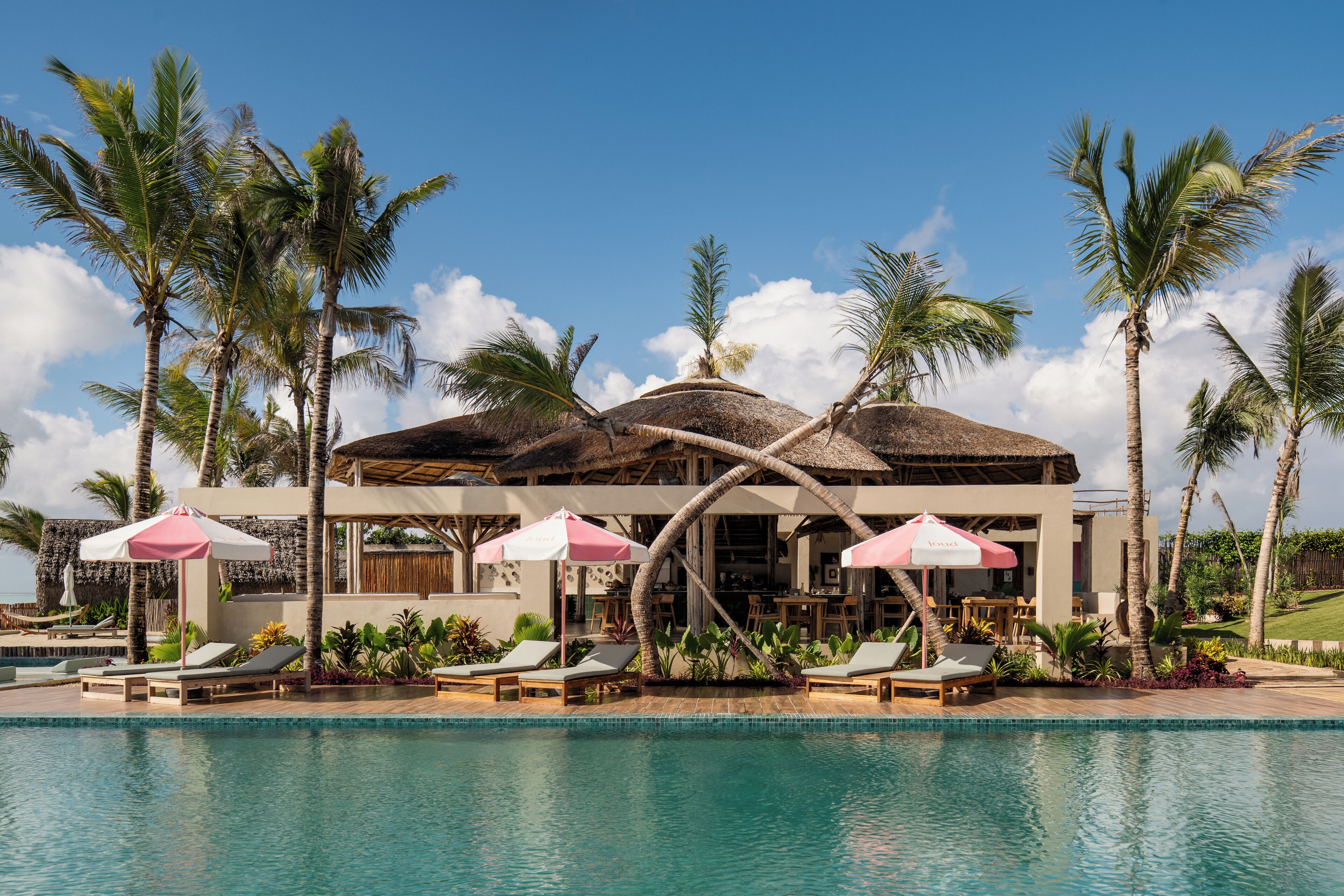 A resort with a pool, lounge chairs, umbrellas, and palm trees.
