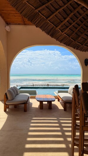 An outdoor seating area with a view of the ocean, a thatched roof, and a pool. - Joud by the sea (Jambiani)