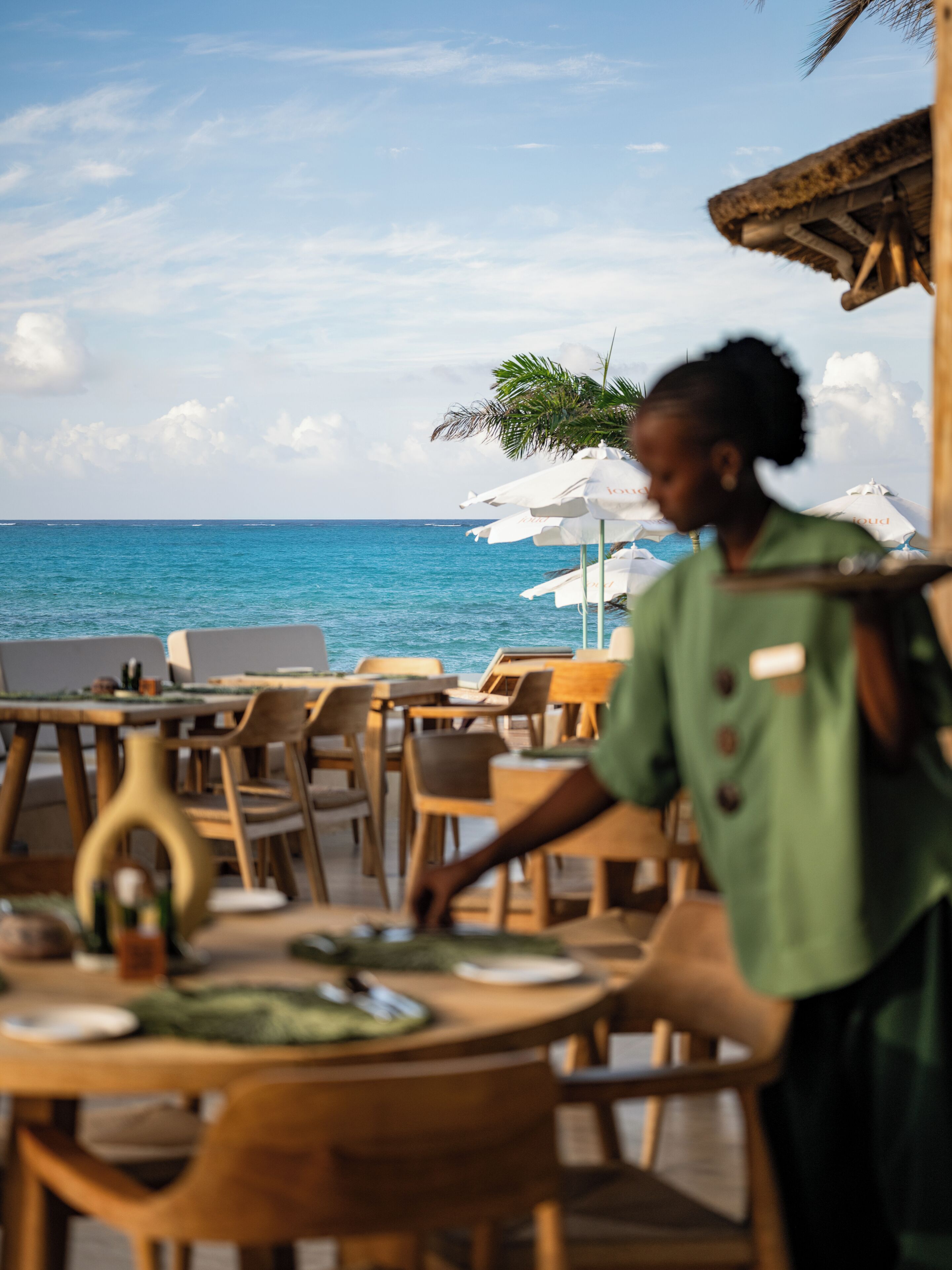 Ein Restaurant direkt am Strand mit Holztischen und -stühlen, Sonnenschirmen und Meerblick.
