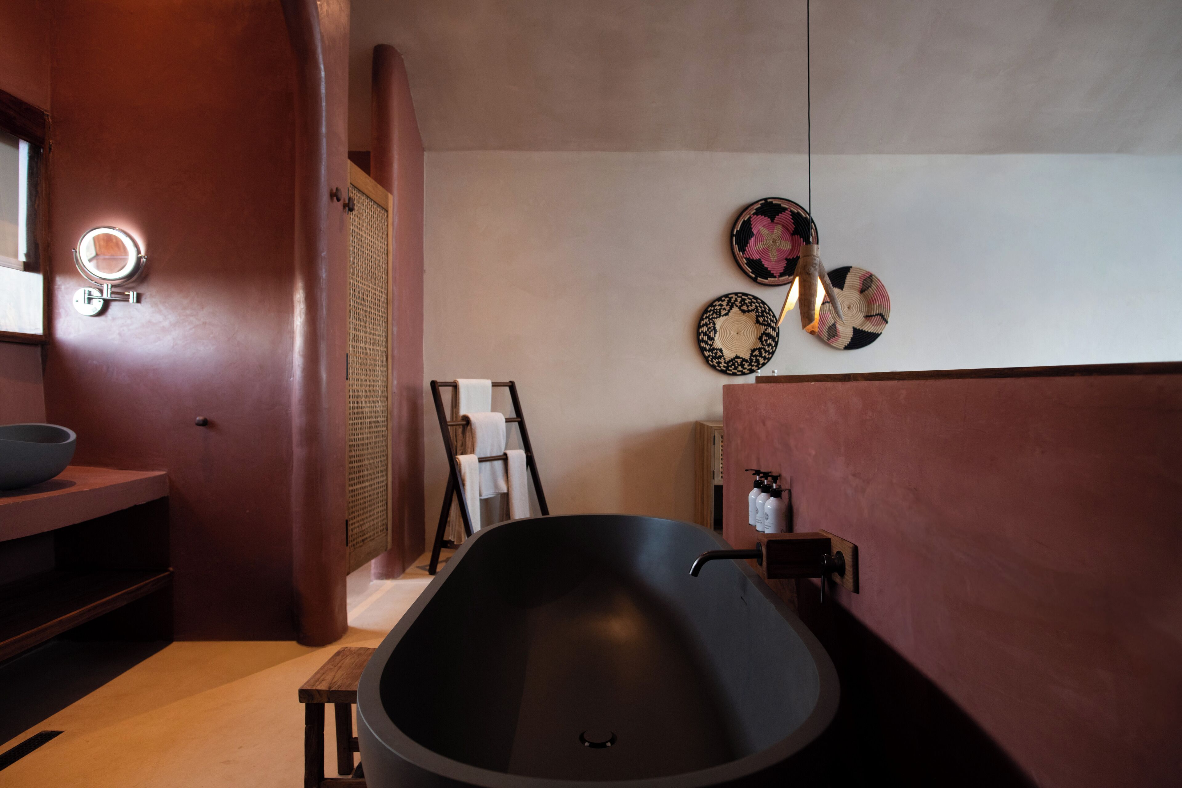 A modern bathroom with a large black bathtub, a wooden vanity, a mirror with a light, and decorative plates on the wall.