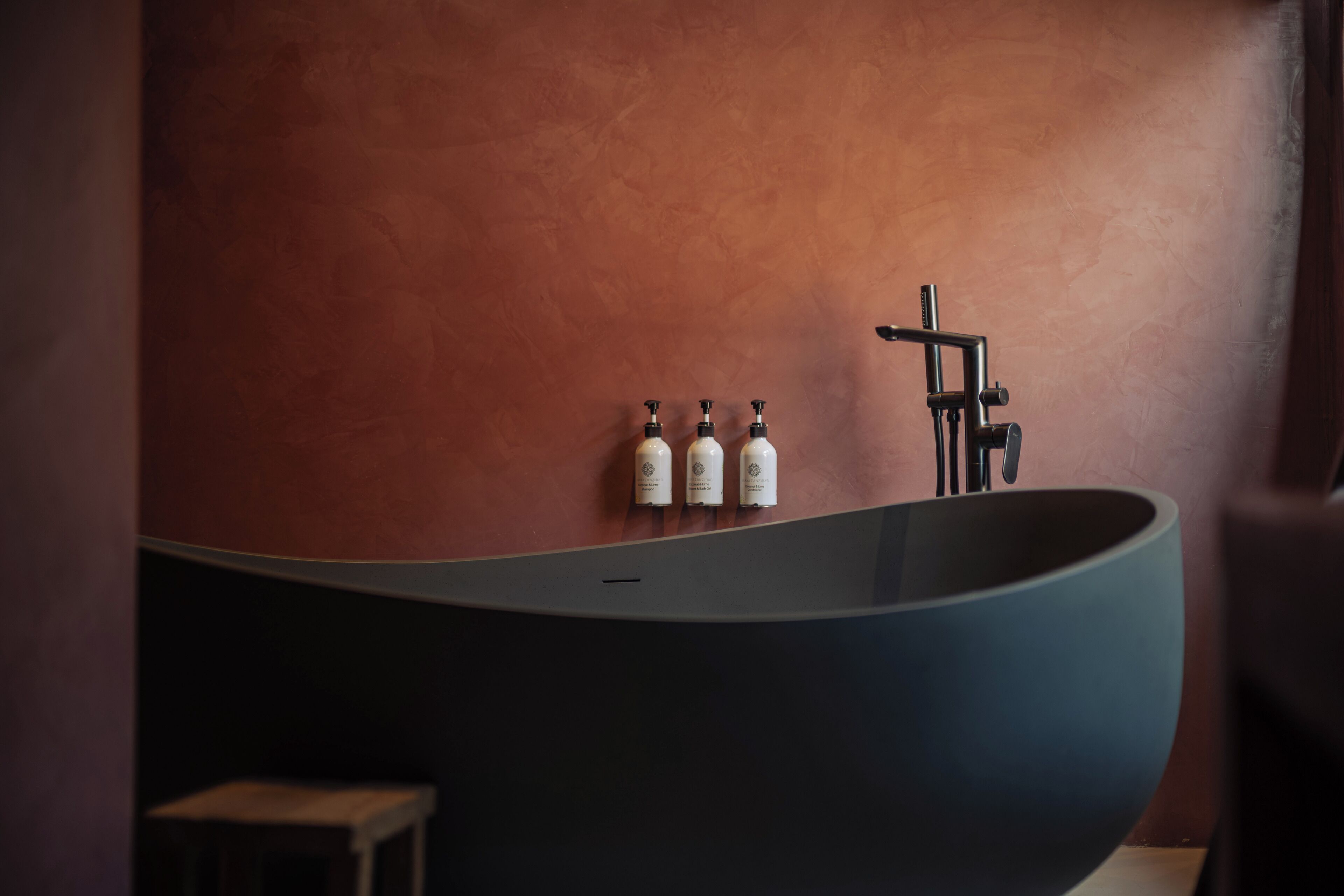 Et moderne badeværelse med et fristående badekar, en vandhane og tre shampoo flasker.