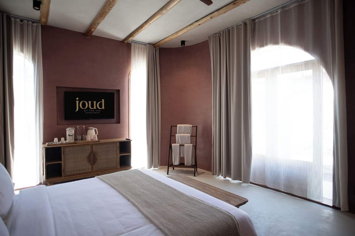 Habitació d'hotel amb un llit, una televisió penjada a la paret, un penjallavops i una finestra amb cortines.