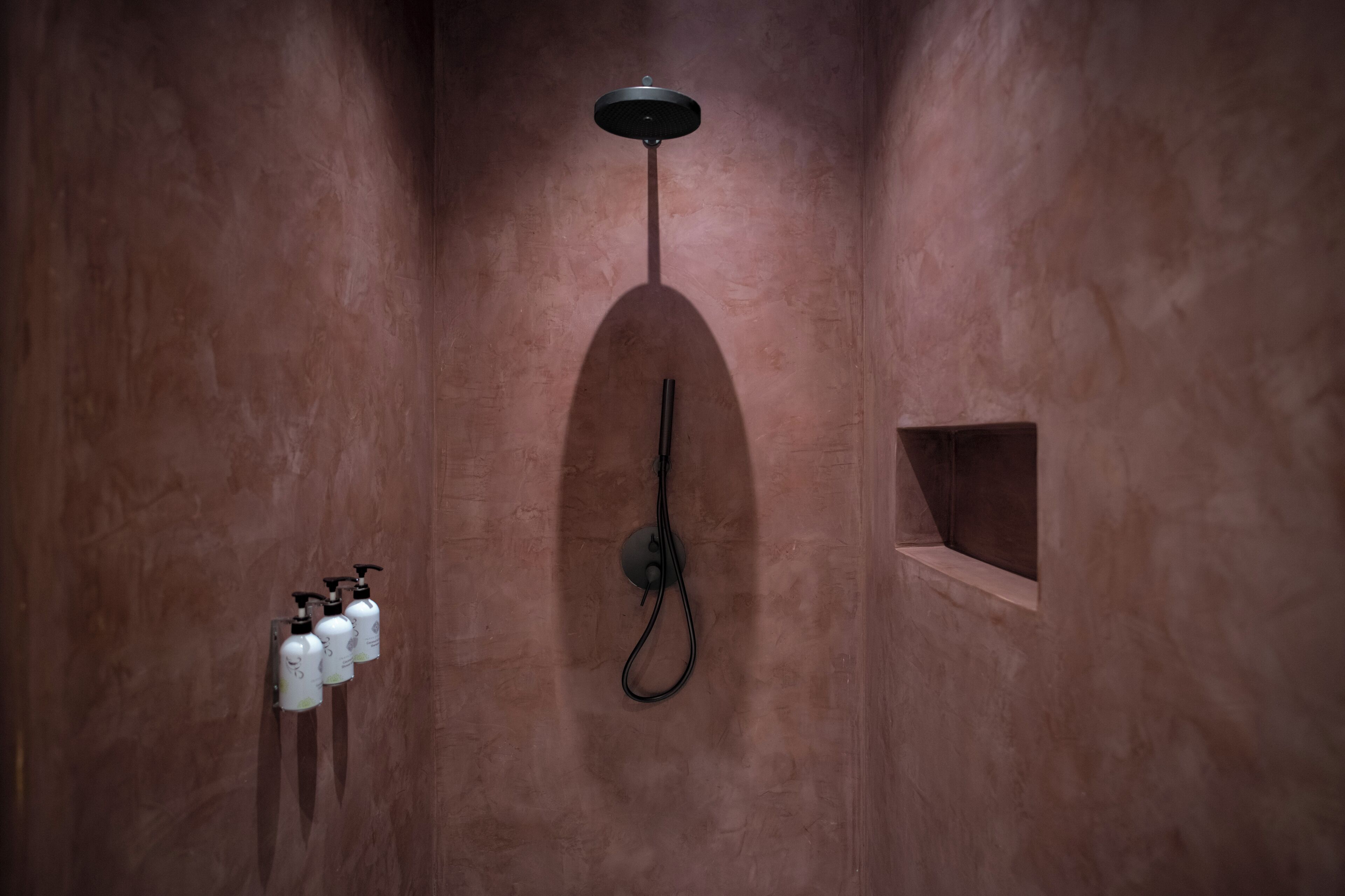 A bathroom with a shower, a towel rack with bottles, and a small shelf.