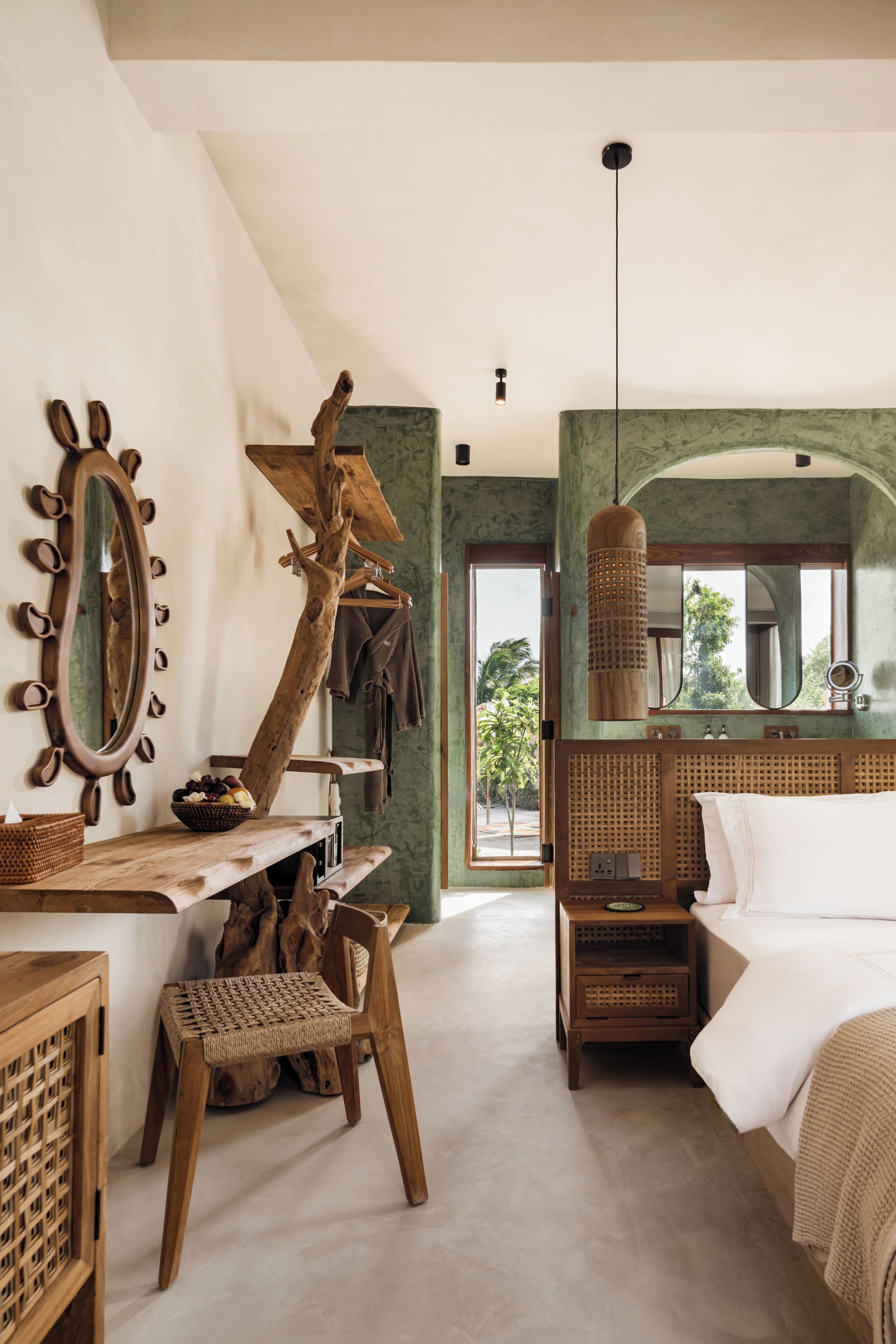 A bedroom with a bed, a wooden chair, a mirror, and a hanging light fixture.
