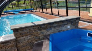A swimming pool with stone walls and a hot tub, surrounded by a covered patio area.
