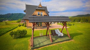 A wooden house with a sloped roof and a swing set in the foreground.