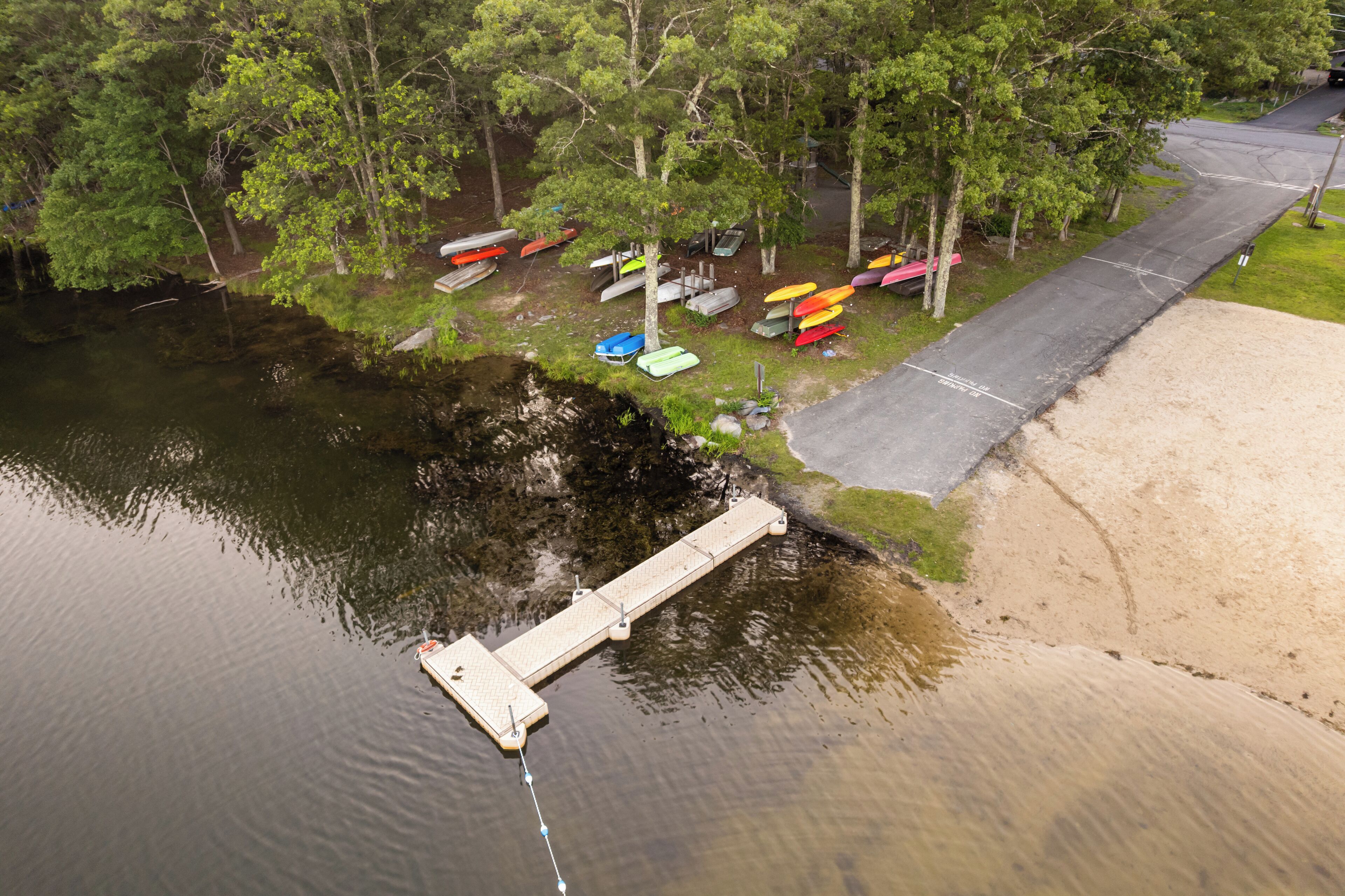 A dock extending into a body of water with several canoes and kayaks stored on the shore.