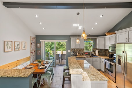 A modern kitchen with granite countertops, stainless steel appliances, and a dining area with a bench and chairs.. Hideaway / Hot Tub / Sunna / Lake / Kayaks / Pool / Game Room / Cold Plunge