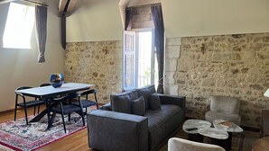 A cozy living room with a stone wall, a gray sofa, a dining table with chairs, and a coffee table. - An enchanting chateau set in 10 hectares of wooded parkland, in absolute peace and quiet! (Les forges)