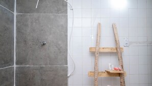 A bathroom with grey tiles, a wooden ladder, and a shelf with toiletries. - Cozy Lakefront Suites RGB (Hidrolandia)