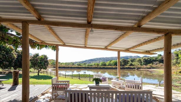 A covered outdoor seating area with wooden benches and tables, overlooking a calm lake and distant hills. - Cozy Lakefront Suites RGB (Hidrolandia)