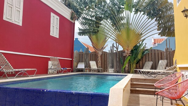 A pool area with lounge chairs, a wooden fence, and a red building.