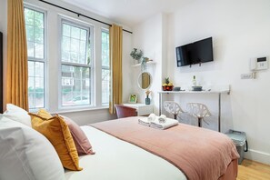 Ein Hotelzimmer mit einem großen Bett, einem Schreibtisch mit Stuhl, einem Fernseher und einem Fenster mit Vorhängen.