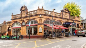 A historic building with a balcony, a sign for 'Baron's Court Station', and a 'District Railway' sign. - Charming Cozy Studio Apartment (London)
