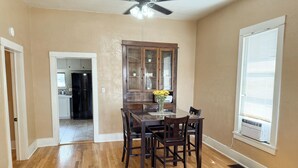Un coin repas avec une table et des chaises en bois, un ventilateur de plafond et une fenêtre avec des stores.