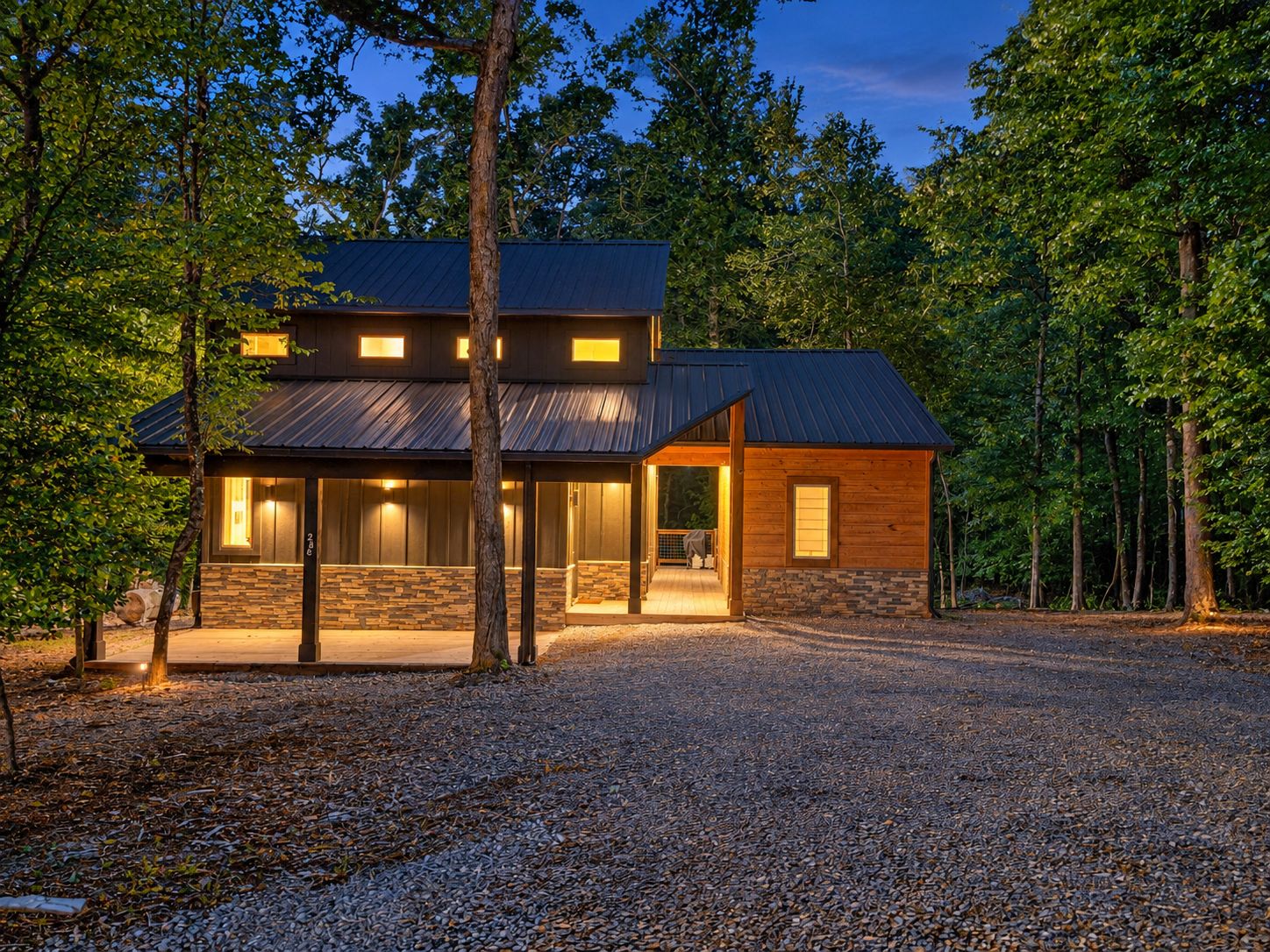 A two-story cabin with a stone foundation and a metal roof, surrounded by trees.