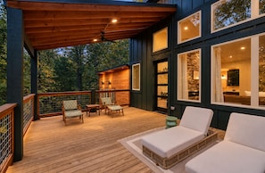 A wooden deck with outdoor seating, a covered area, and large windows. - Ride ATVs • Luxe King Suite • EV Charger • Prime Location • Sleeps 10 (Broken Bow)