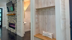 A modern interior with a stone accent wall, a fireplace, and a sign reading "Hochatown Oklahoma." - Ride ATVs • Luxe King Suite •  Modern-Meets-Cozy Retreat  • Prime Location (Broken Bow)