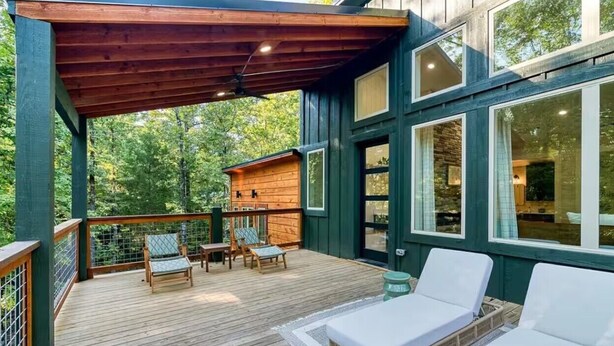 A wooden deck with outdoor seating, a covered area, and large windows. - Ride ATVs • Luxe King Suite •  Modern-Meets-Cozy Retreat  • Prime Location (Broken Bow)