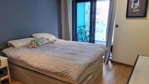 Een slaapkamer met een bed, een bureau, een stoel, een raam met gordijnen en uitzicht op de omgeving.