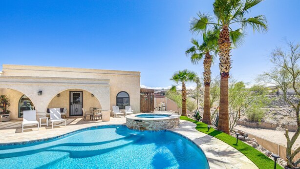 A swimming pool with a hot tub, lounge chairs, and palm trees.