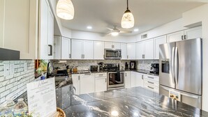 A modern kitchen with white cabinets, a stainless steel refrigerator, a microwave, and a large island with a black marble countertop.