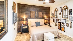 A bedroom with a large bed, wooden wall paneling, and multiple framed artworks.
