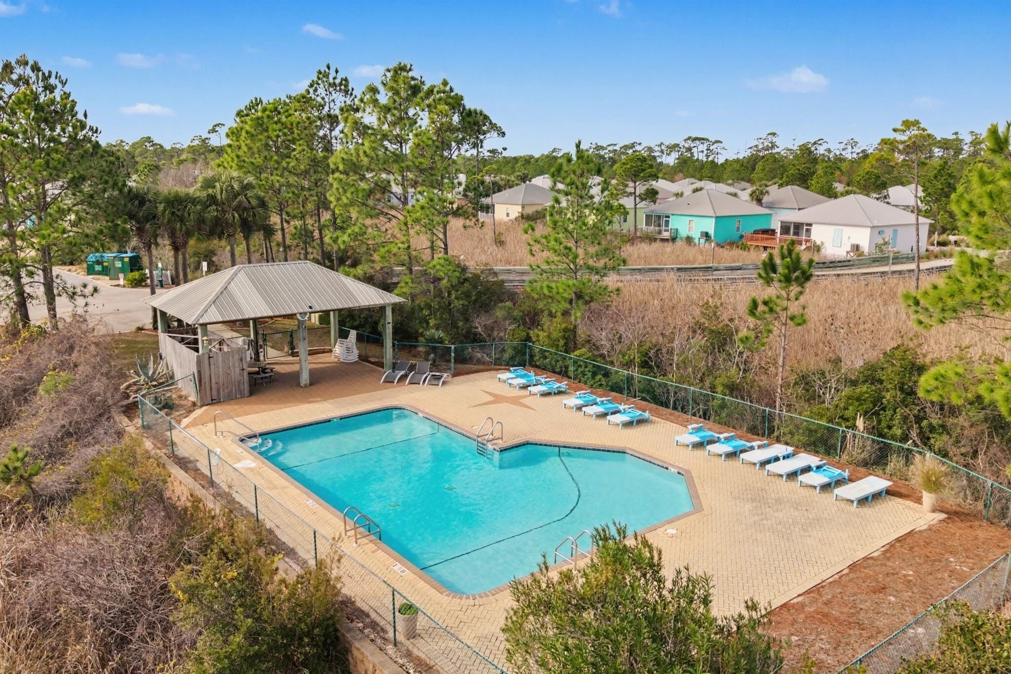 A swimming pool with lounge chairs, a covered seating area, and houses in the background.