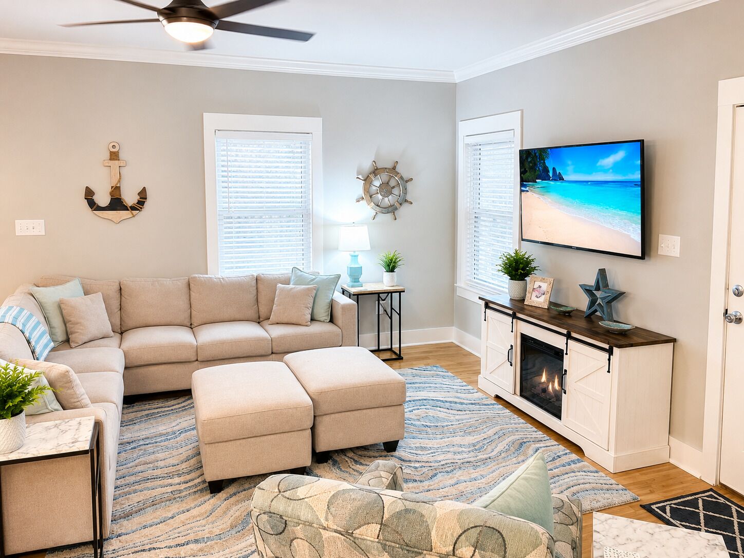 A living room with a sectional sofa, ottoman, a flat-screen TV, a fireplace, and a ceiling fan.