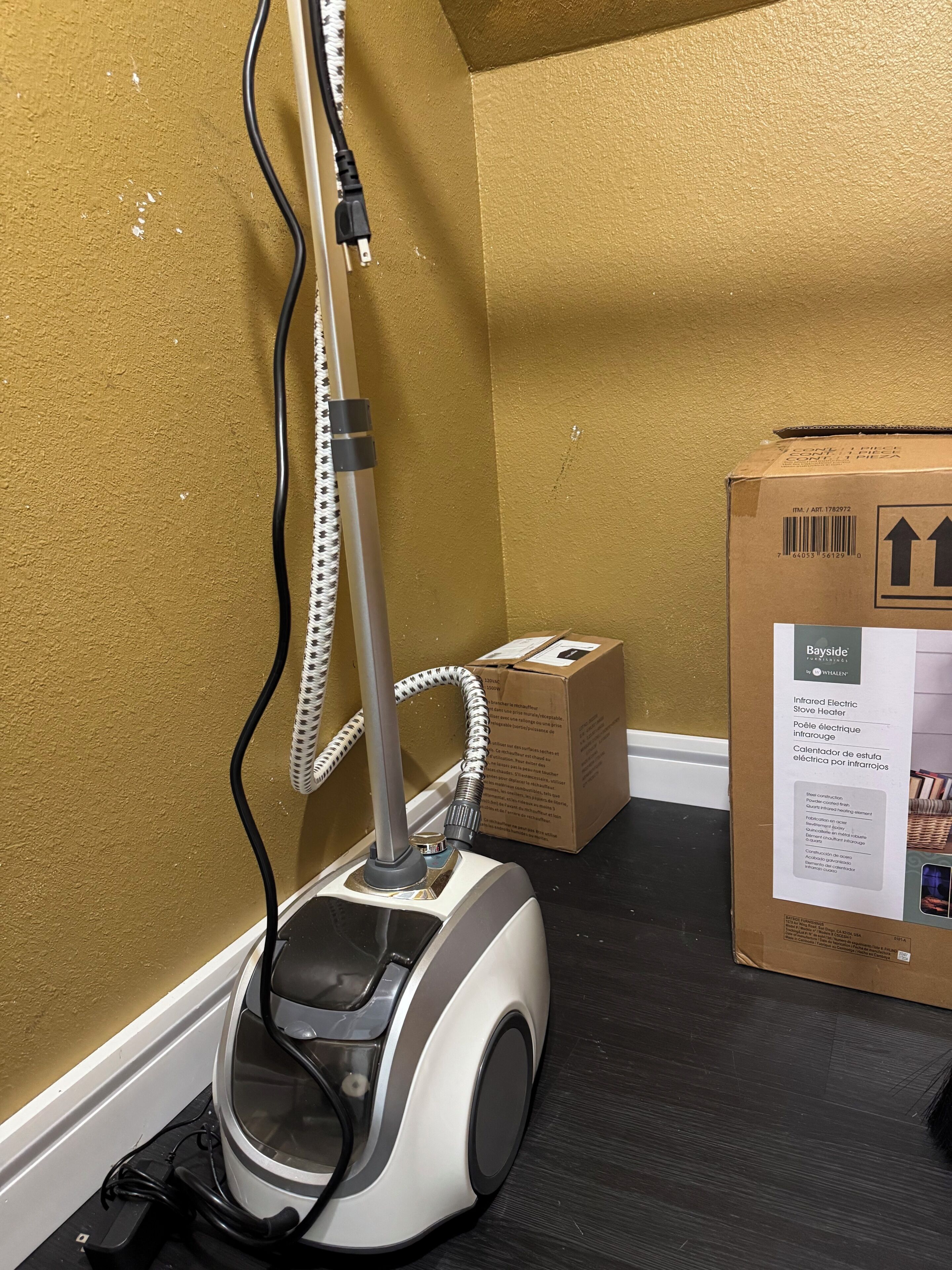 A vacuum cleaner with a hose and power cord, a cardboard box, and a wall with a textured surface.