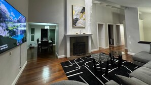 Ein modernes Wohnzimmer mit Flachbildfernseher, Kamin, Essbereich und einem Gang, der in einen anderen Raum führt.