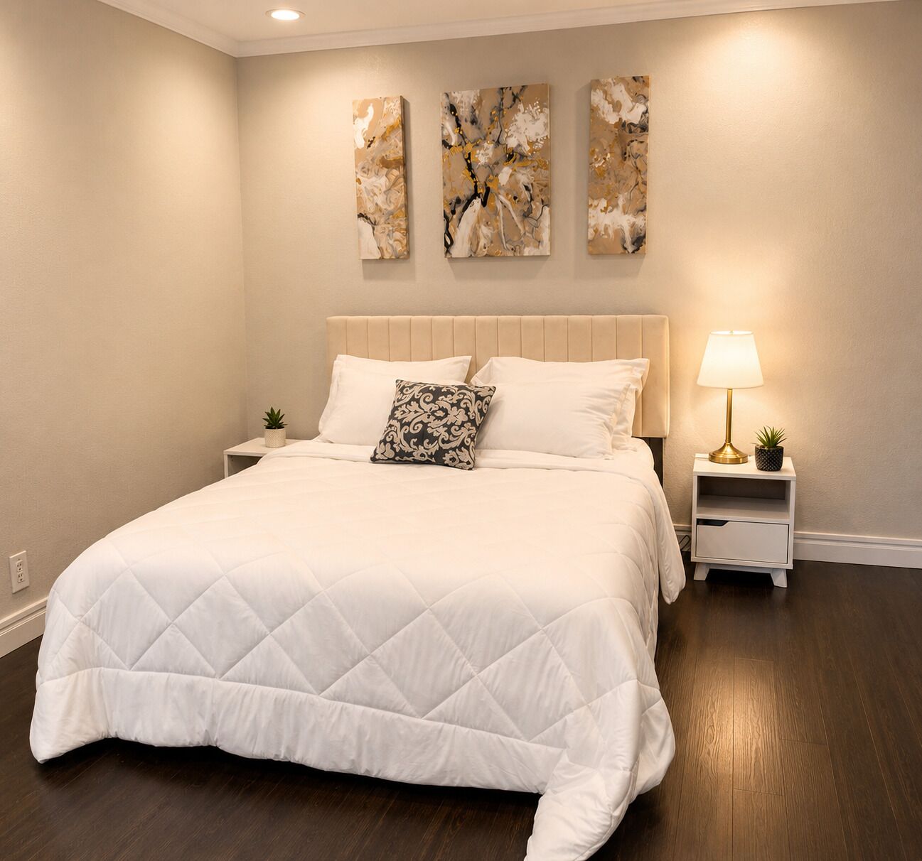 A bedroom with a large bed, a nightstand with a lamp, and three wall art pieces.