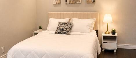A bedroom with a large bed, a nightstand with a lamp, and three wall art pieces.