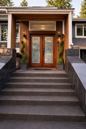 A modern house with a wooden front door, two wall-mounted lights, and a stone staircase leading to the entrance. - Seattle Escape Hot Tub,Sauna,Gym, Game Room, EV charging, massager,GROUPS (Sammamish)