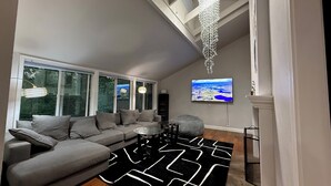 Ein modernes Wohnzimmer mit einem grauen Sofa, einem schwarz-weißen Teppich, einem runden Couchtisch und einem an der Wand montierten Fernseher.